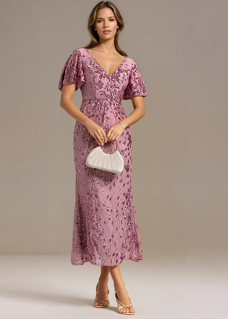 Woman wearing a pink lace dress holding a white clutch against a neutral background