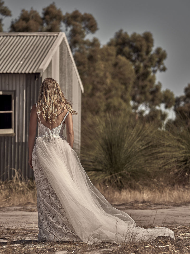 Woman in a white dress standing in a rustic outdoor setting with a wooden cabin and trees.