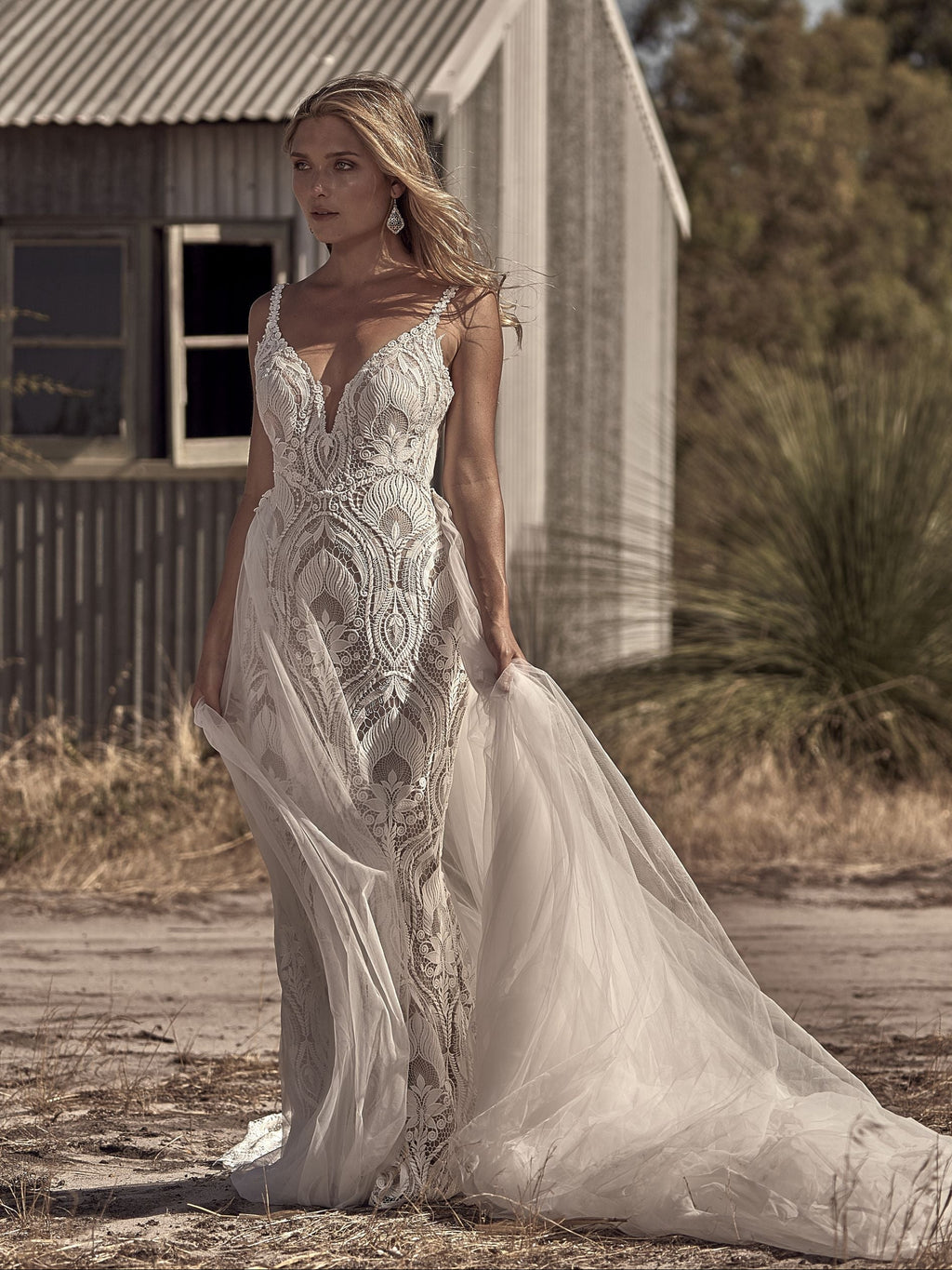 Woman in a white wedding dress standing in front of an old building with trees in the background