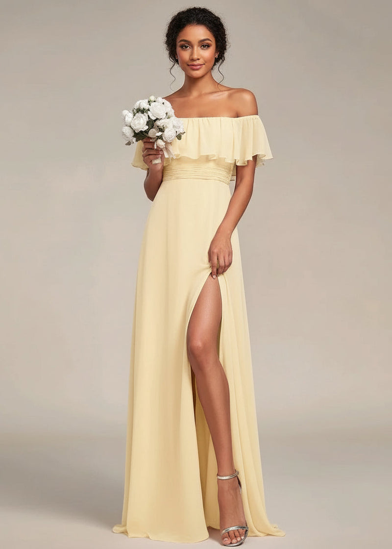 Woman wearing a yellow off-shoulder dress with a slit, holding flowers against a neutral background